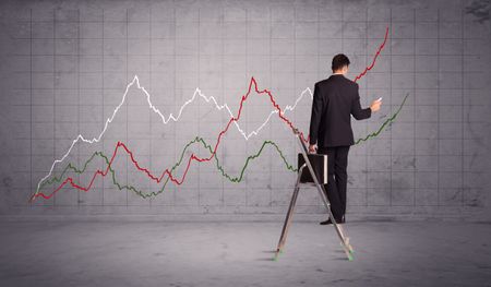 A guy in modern suit standing on a small ladder and drawing a chart on grey wall background with exponential progressing curves, lines