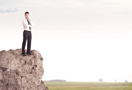 A successful good looking business person standing on top of a high cliff above country landscape with clear white sky concept