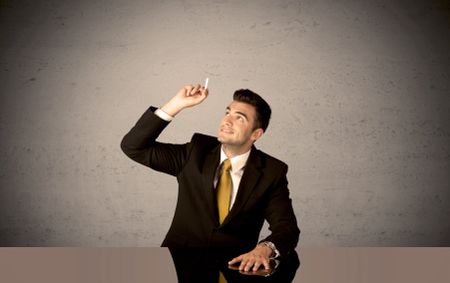 A happy businessman sitting at desk in front of clear grey empty background and drawing around himself with a white chalk concept