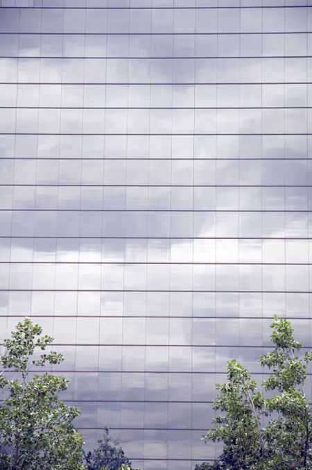 Sky of glass - tree tops at bottom of skyscraper with mosaic of windows reflecting heavy clouds