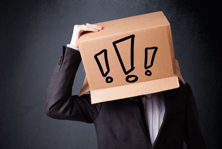 Businessman standing and gesturing with a cardboard box on his head with exclamation point