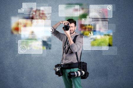A young professional male photographer holding cameras and taking pictures in front of a blue wall with pictures, icons, text information concept