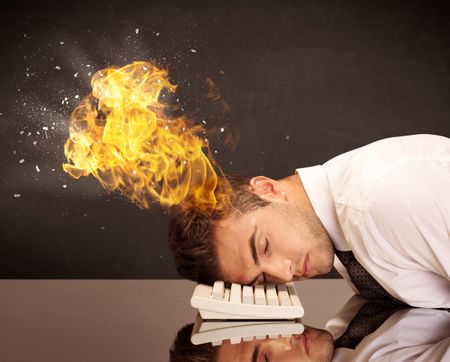 A depressed businessman banging his head in a keyboard and shouting with his head on fire, reflecting on desk