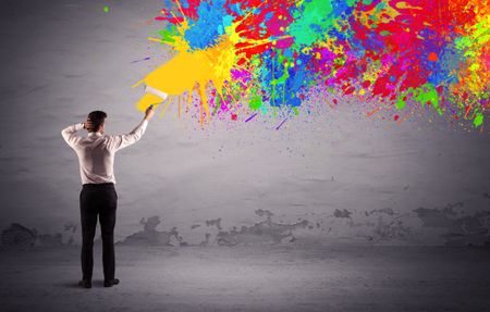 An elegant businessman in suit painting colorful splatter, bright colors on grey urban wall with a paint roller in his hand concept