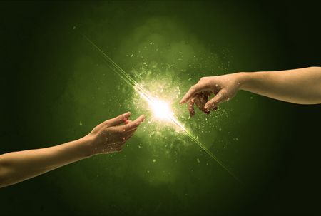 Two naked male hands about to touch, lighting the spark with modest explosion in front of green background concept