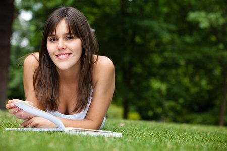 Beautiful young woman reading a book at the park