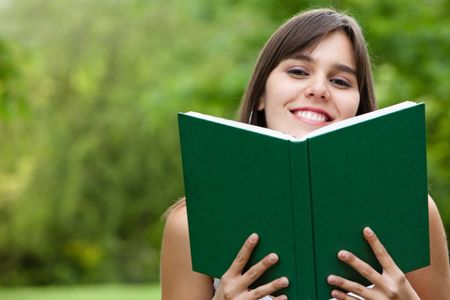 smiley young woman holding a book outdoors