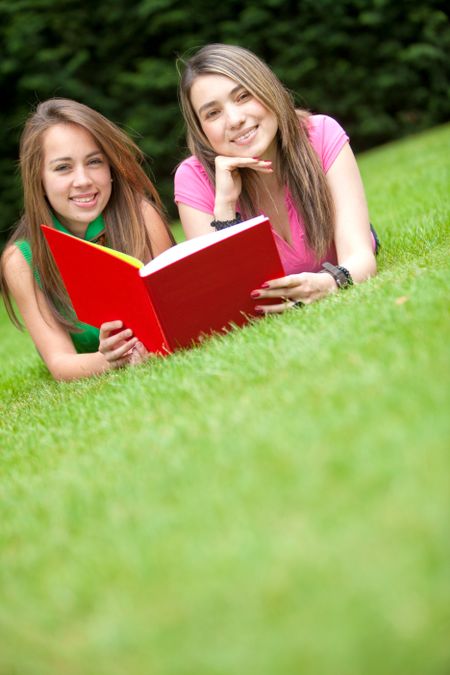 Beutiful girls reading a book outdoors and smiling