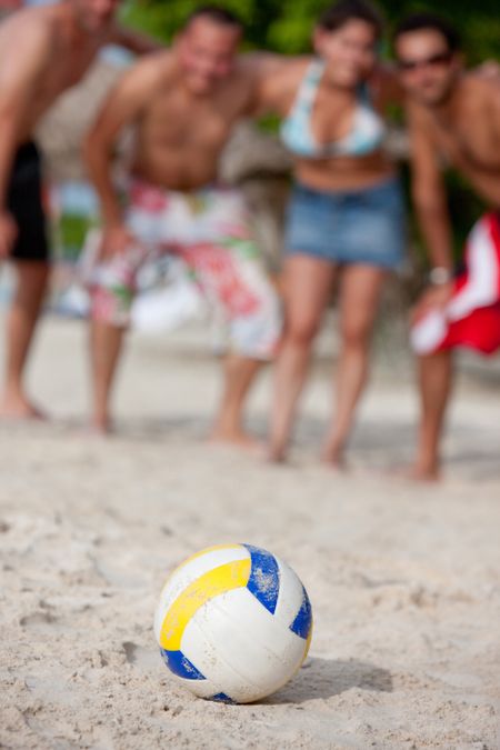 Beach volleyball lying over sand and people behind it