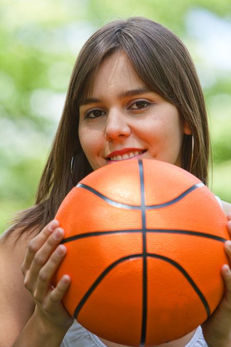 Smiley young woman holding a basketball outdoors
