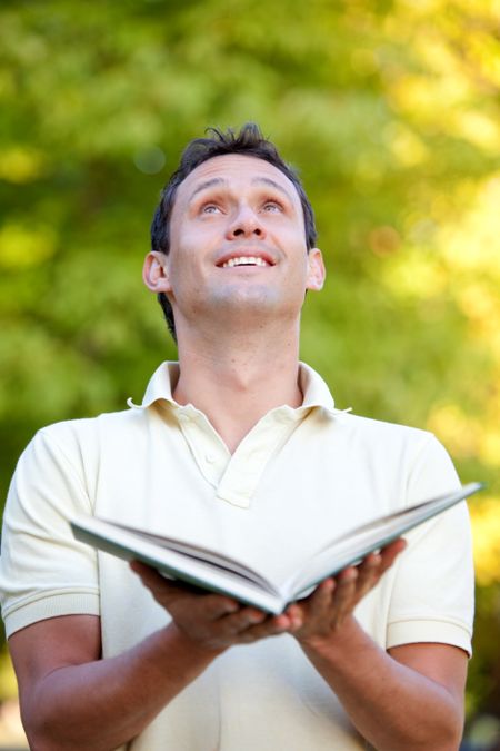 Man outdoors holding a book and looking up