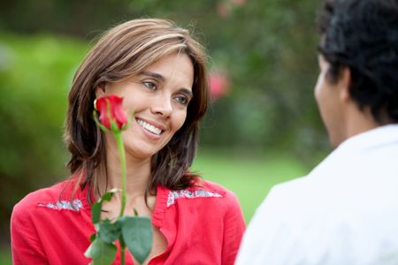 Beautiful woman getting a red rose from his partner outdoors