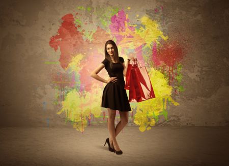 A happy young elegant woman standing with shopping bags in front of brown wall background full of colorful ink splatter concept
