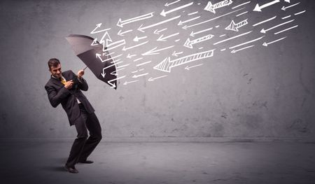 Business man standing with umbrella and drawn arrows hitting him on grungy background