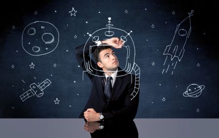 A young happy businessman in elegant suit drawing helmet, satellite and rocket in empty space with a chalk illustration concept