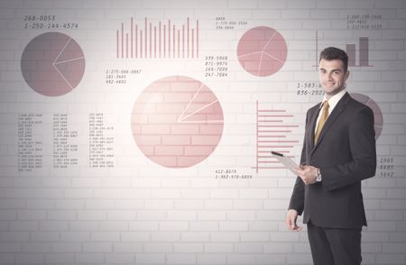 Young sales business male in elegant suit standing in front of brick wall background with lines and pie charts concept