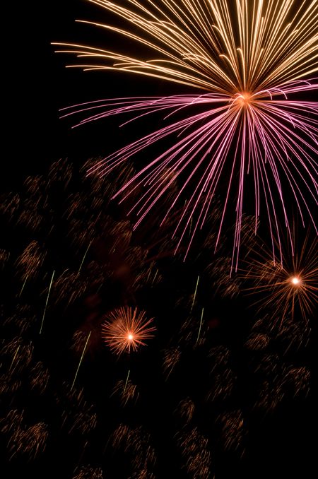 Pink and whitish burst of fireworks above smaller bursts and embers