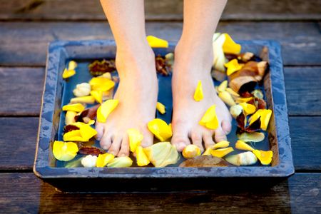 woman putting her feet into water with flowers - beauty concepts
