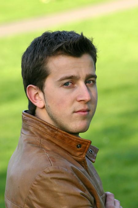 casual guy posing in a park wearing a leather jacket