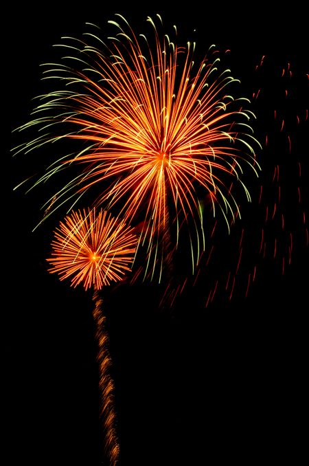 Two bursts of reddish orange fireworks, the larger one with yellowish white tips by fading red sparks at right