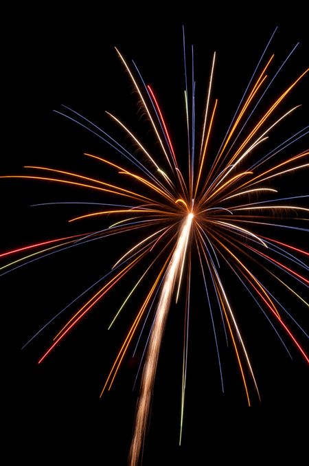 Multicolored burst of fireworks with white rocket trail