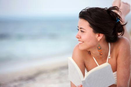 Beautiful woman lying at the beach with a book
