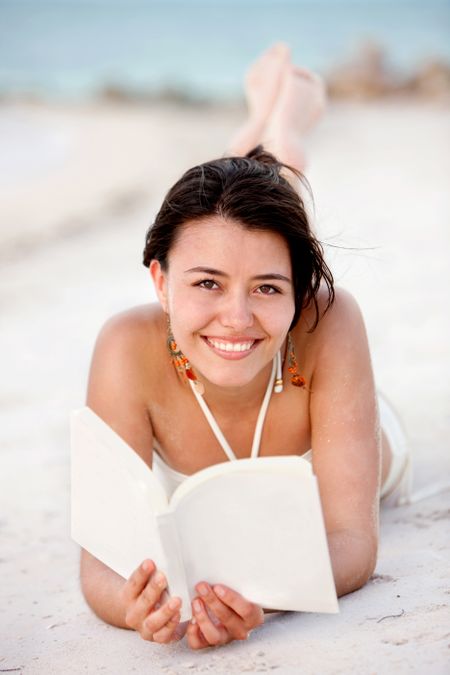 Beautiful woman lying on the beach with a book