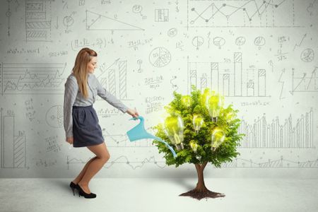 Business woman pouring water on lightbulb growing tree concept