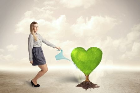 Business woman watering heart shaped green tree concept on background