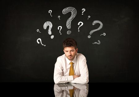 Depressed businessman sitting under question marks