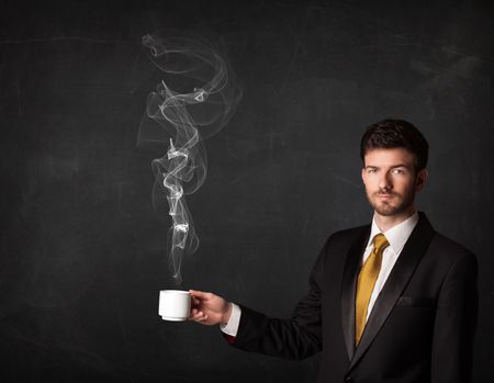 Businessman standing and holding a white steamy cup on a black background 