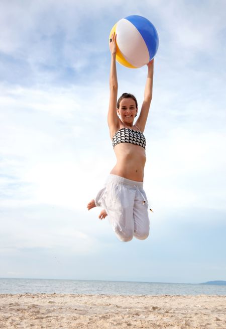 Girl at the beach jumping with a ball