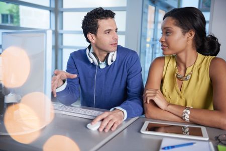 Two  colleages discussing ideas using a tablet and computer