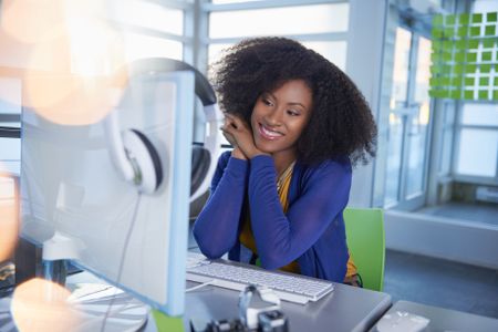 Portrait of a smiling woman with an afro at the computer in bright glass office