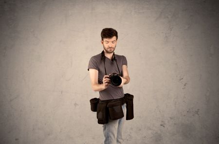 A professional male photographer with belt holding a camera and taking photos in front of clear grey urban wall background concept