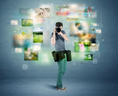A young amateur photographer with professional camera equipment taking picture in front of blue wall full of faded pictures and glowing lights concept