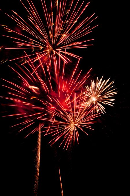 Fireworks bursting near one another with reddish smoke