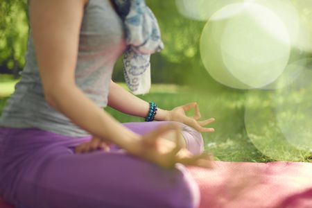 Serene and peaceful woman practicing mindful awareness by meditating in nature at sunset with background bokeh.