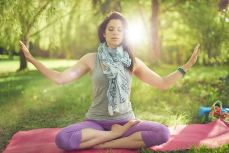 Serene and peaceful woman practicing mindful  awareness by meditating in nature with sun flare.