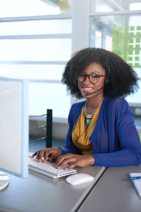 Portrait of a smiling customer service representative with an afro at the computer using headset