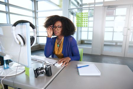Portrait of a smiling woman with an afro at the computer in bright glass office