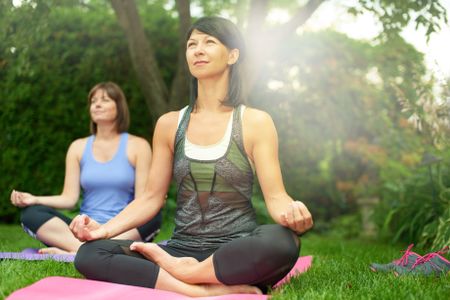 Two mature women keeping fit by doing yoga in the summer