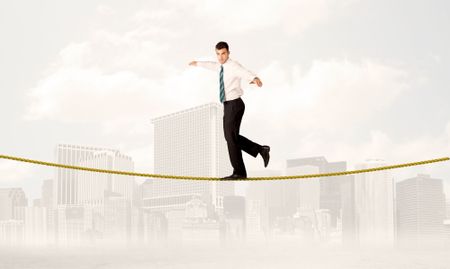 A young elegant businessman walking on tight golden rope in front of city buildings landscape background concept