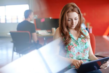 Confident female designer working on a digital tablet in red creative office space