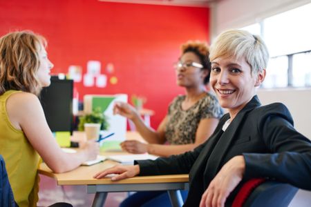 Confident female designer sitting at her desk for a brainstorming in red creative office space