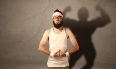 A funny young guy posing in front of brown background with musculous body shadow reflected on the wall 