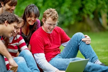 Group of friends with a laptop smiling outdoors