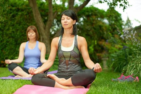 Two mature women keeping fit by doing yoga in the summer