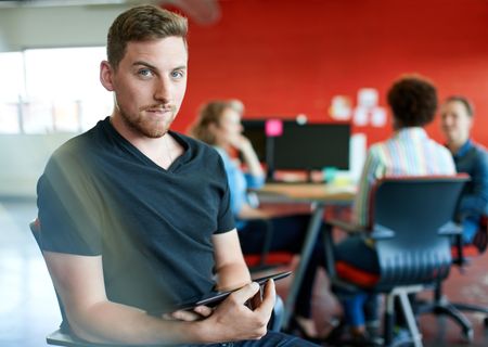 Confident male designer working on a digital tablet in red creative office space