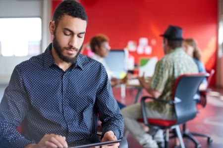 Confident male designer working on a digital tablet in red creative office space